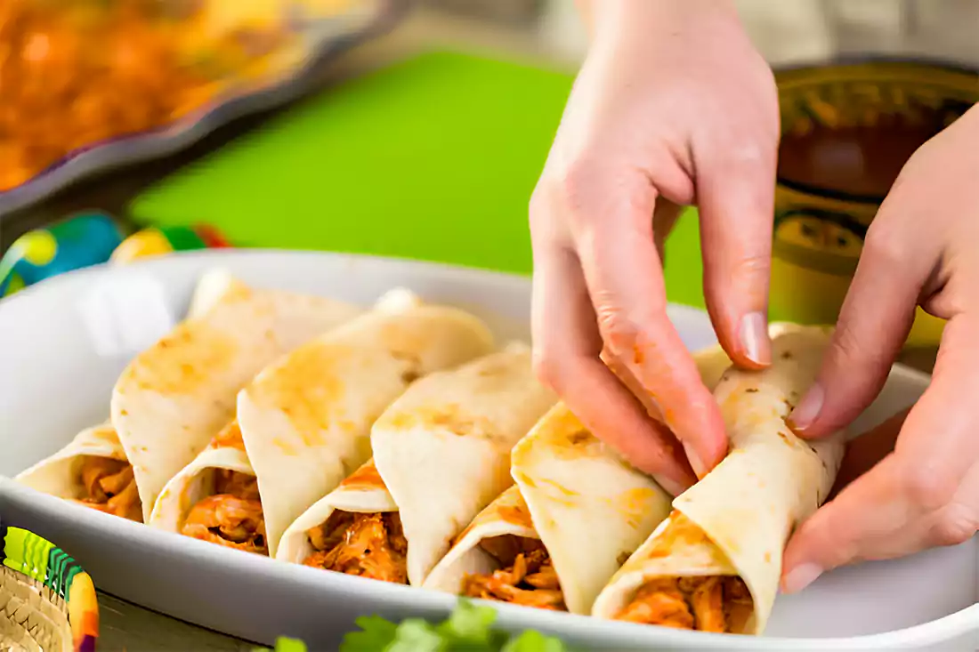 Hands assembling chicken tacos in a kitchen setting, showcasing the filling and folding process