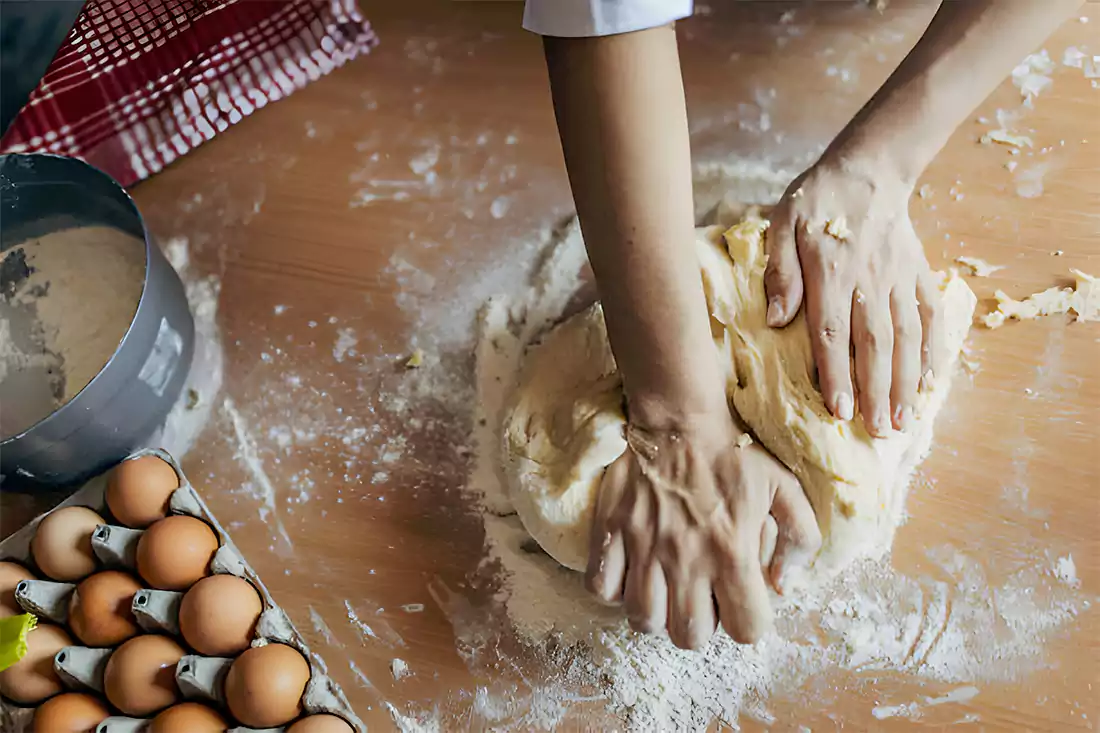 Hands kneading dough on a floured surface in preparation for cinnamon bread