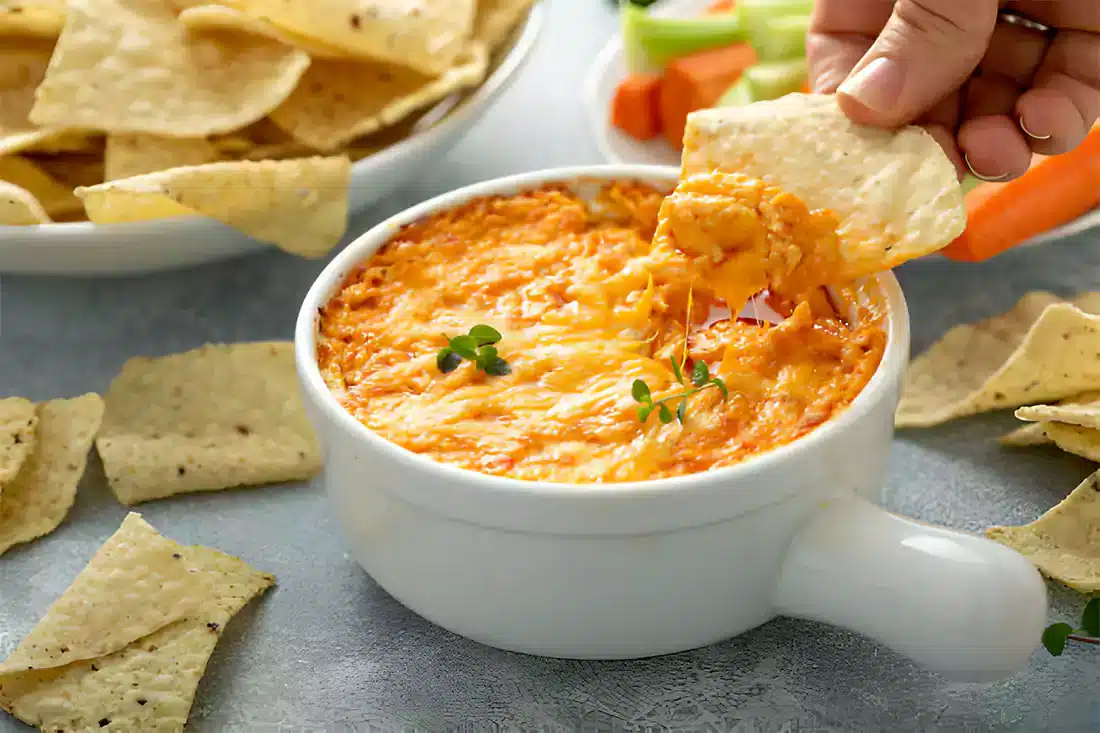 A vibrant serving of Buffalo Chicken Dip accompanied by tortilla chips, celery, and carrots, perfect for sharing.