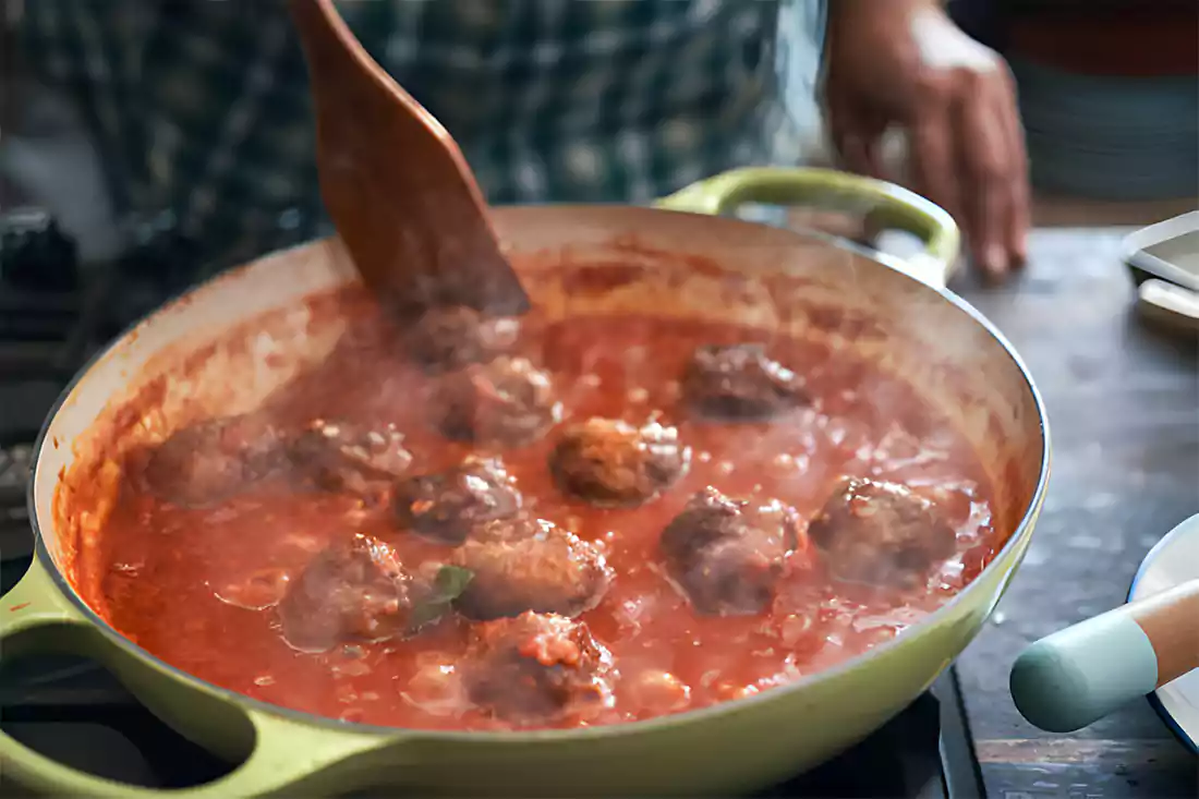 Cooking porcupine meatballs in tomato sauce in a pan, showcasing cooking techniques